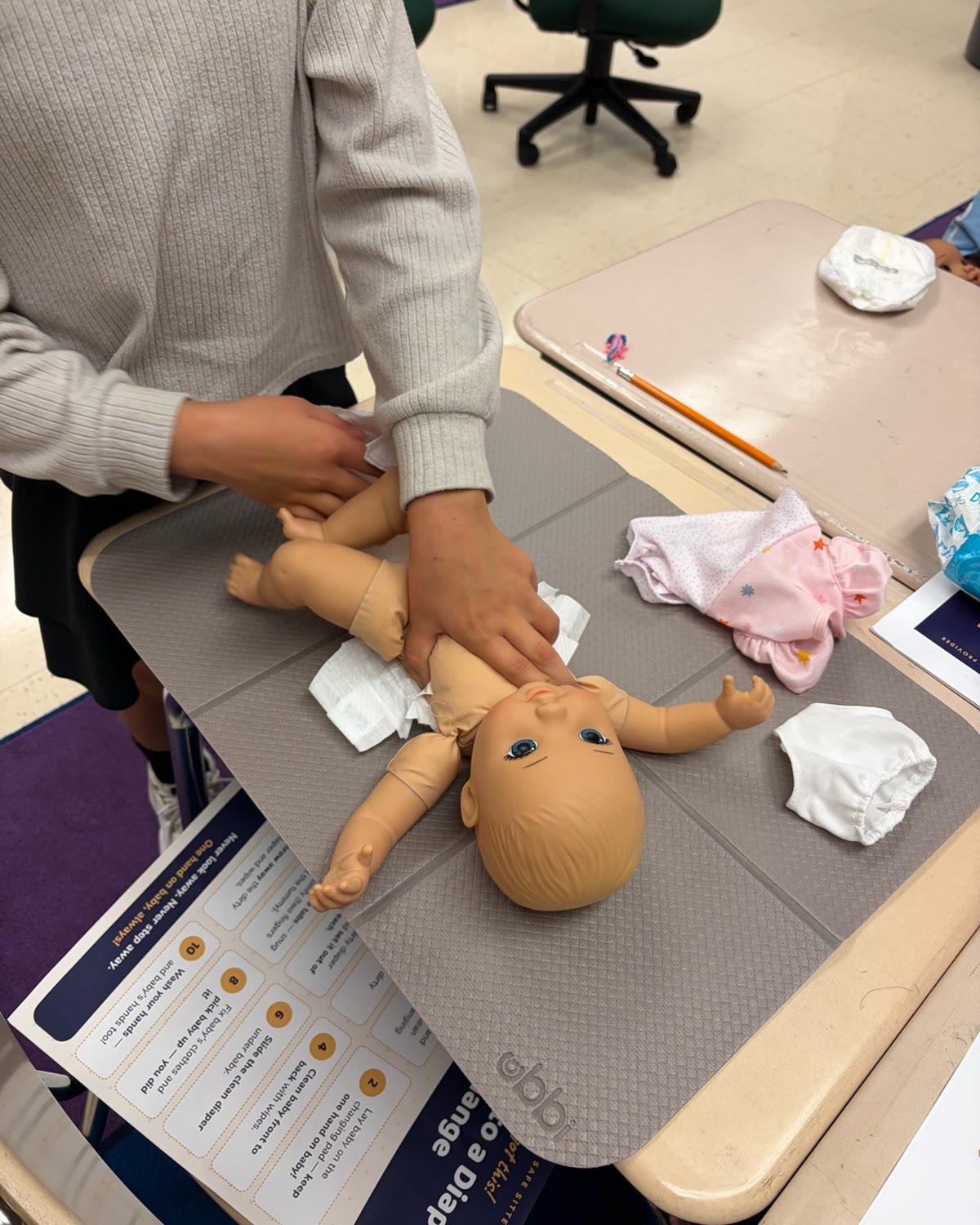 A young student practicing diaper changing in class